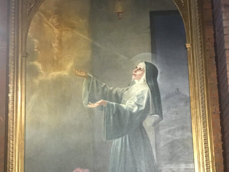 Santa Rita de Casia en oración, con hábito agustino, ante el crucifijo del que sale un rayo de luz