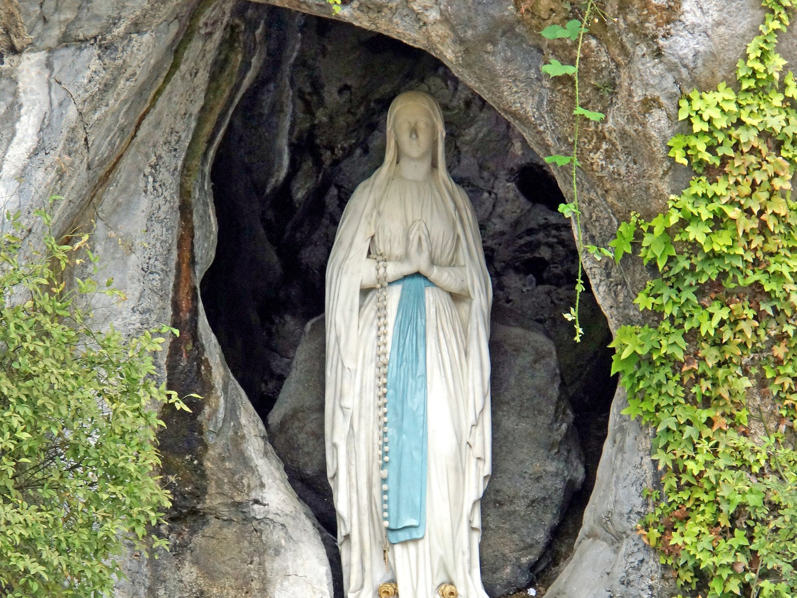 Estatua de la Virgen de Lourdes en la gruta de Massabielle, con cinturón azul y el rosario